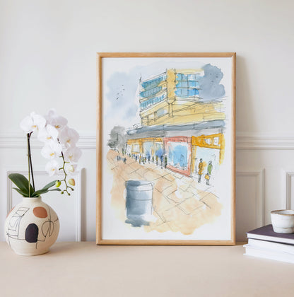Framed watercolour print of 1990s Sunderland town centre displayed on a wall, capturing the bustling high street and iconic tower blocks of a North East city in its prime